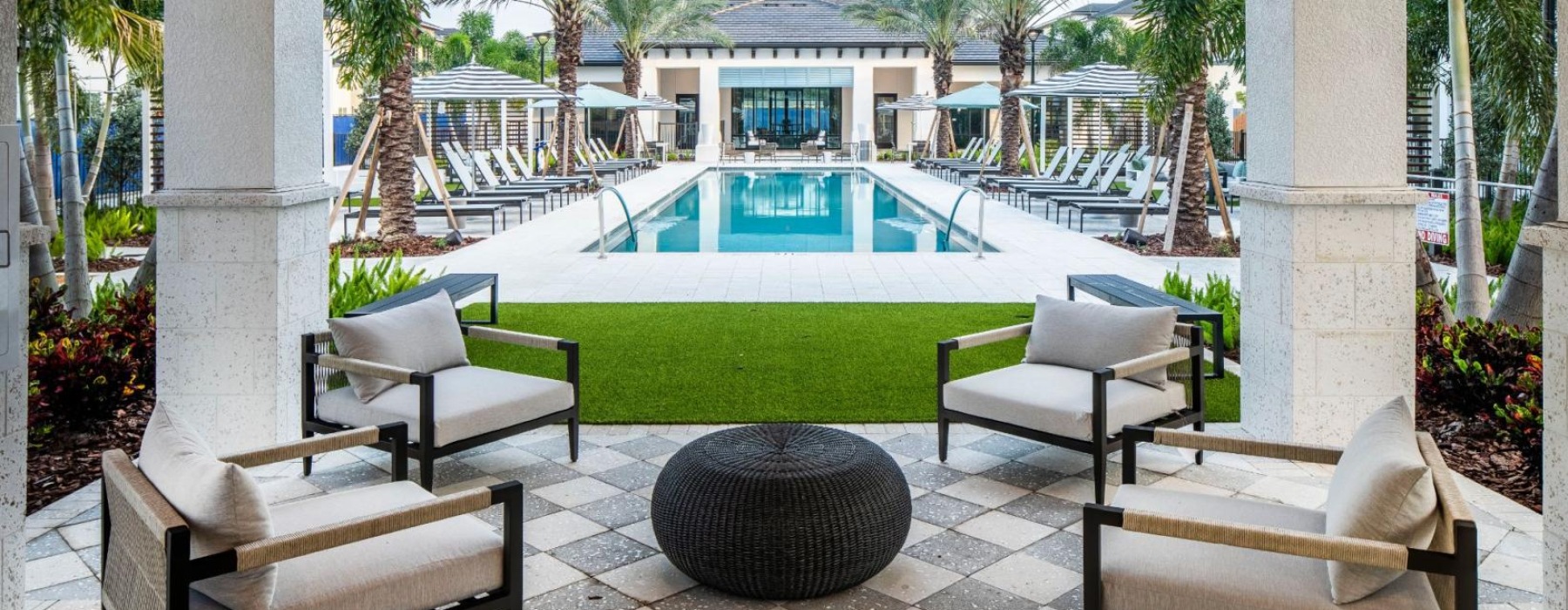 a swimming pool with chairs and a deck with trees and a building in the background at The Shores at Lake Howell Apartments in Casselberry, FL